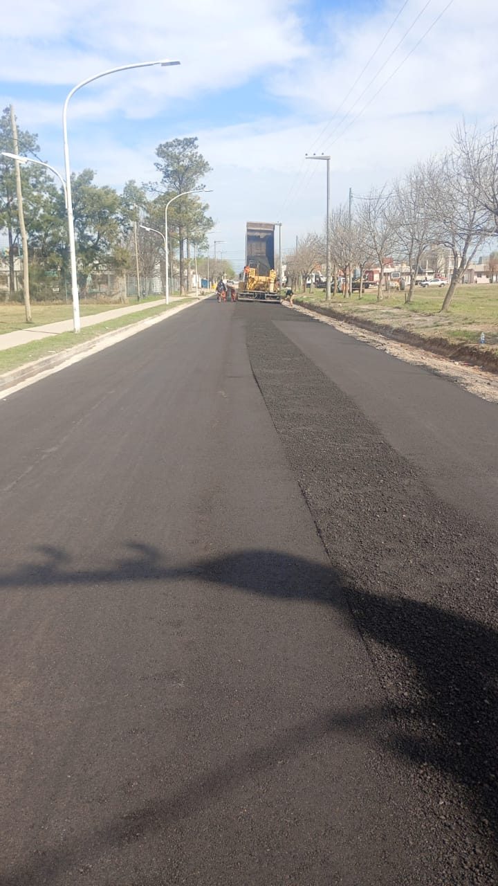 Avenida recién pavimentada con la terminadora avanzando de fondo